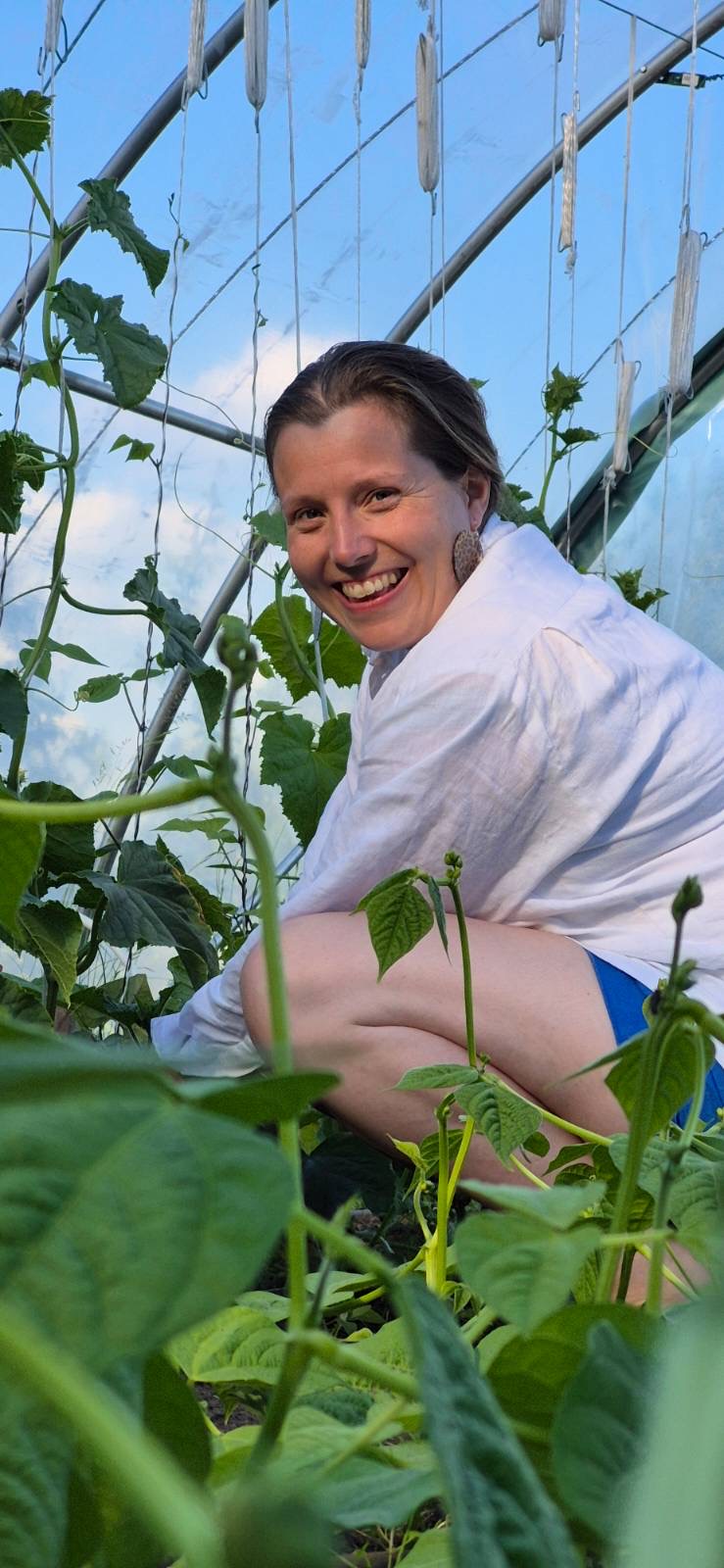 Holly Gurling smiling among bean plants in a polytunnel